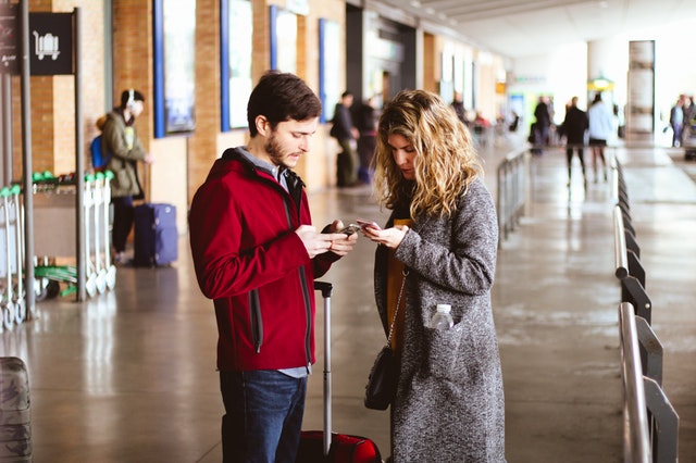 Muž a žena na letisku, ktorí pozerajú do mobilných telefónov